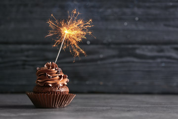 Tasty chocolate cupcake with sparkler on wooden background