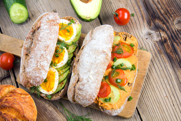 Fototapeta na wymiar Sandwiches with avocado, eggs and tomato on a wooden background. Fresh organic vegetables, eggs and whole wheat bread. Healthy breakfast. Retro style.