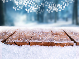 Wooden table, bench covered in snow with a Christmass, wintery and snowy background with space to add products and text.
