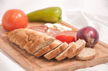 Bread slices , vegetables and prosciutto on a wooden cutting board