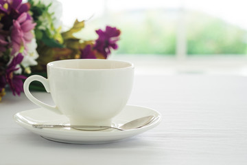 Cup of black coffee placed on white table flower and blurry garden background.