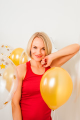 Young blonde woman in red t-shirt is smiling at the background of golden balloons. Celebrating the New Year, Christmas, Birthday Party. Close up