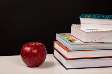 Back to School Concept, Stacked books, and red apple isolated on black background with place for your text