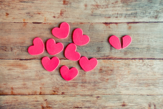 Many red hearts on left side and broken heart on the right side on wooden background. Valentines day concept for heartbroken.