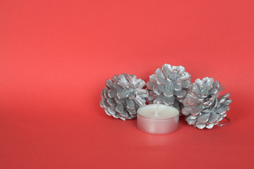 Silver painted pine cones with candle on red background.