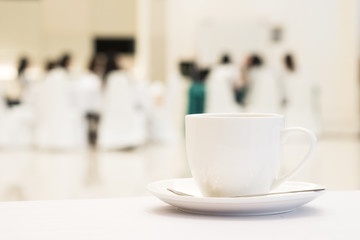 White cup of coffee placed on white table with blurred people have seminar in meeting room background.