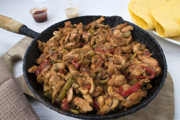 Chicken stew with red and green pepper, with red onion, pickled cucumber and spices in a frying pan.