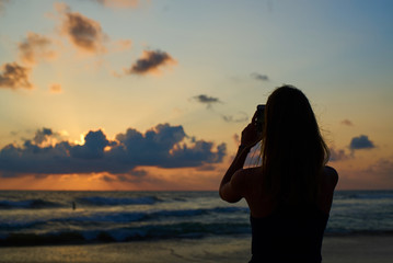 silhouette of young attractive female making photo of sunset by smartphone