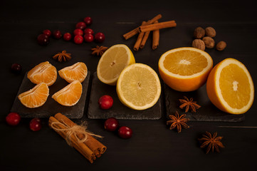 Obraz na płótnie Canvas Orange, half orange, lemon, half lemon, mandarin, slices of tangerine with cinnamon, cranberries, nuts and anise on a black background