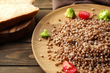 Plate with tasty buckwheat porridge and vegetables on table, closeup