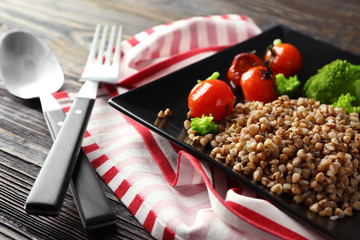 Plate with tasty buckwheat porridge and vegetables on wooden table