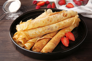 Plate with delicious thin pancakes on table