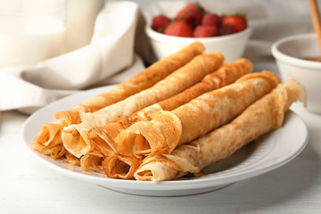 Plate with delicious thin pancakes on table