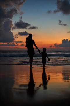 silhouette of mother carrying daughters front of beautiful ocean beach sunset