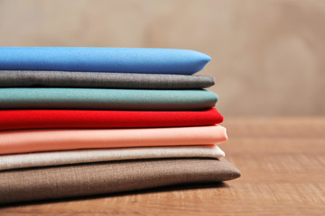 Stack of colorful fabrics on wooden table, closeup