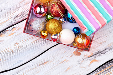 Different shiny Christmas balls in gift box. Christmas decoration toys in open striped gift box on vintage wooden background, top view.