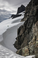 A mountaineer climbs up a glacier, dwarfed by rocky peaks