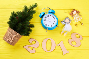 New Year and Christmas wooden background. Wooden number 2018, alarm clock, little spruse and Christmas tree angels on yellow wooden background. Happy New Year 2018.
