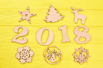 Number 2018 and wooden New Year figures. Christmas background with decorations. Wooden handmade carved figures of star, deer, spruce, candles on colored background.