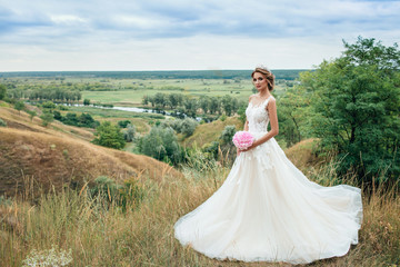 Fototapeta na wymiar Beautiful young bride girl smiling, standing in wedding dress. Overlooking the beautiful green valley.