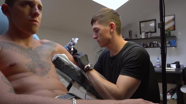 Adult guy bravely suffers when a tattoo artist causes him discomfort and little pain