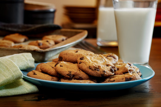 Plateful of chocolate chip cookies fresh and warm out of the oven with cold glass of milk