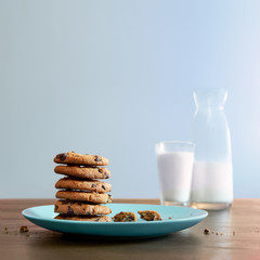 Warm chocolate chip cookies stacked on a plate with glass of cold milk on old wood table