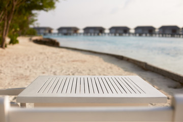 Empty top of white wooden table for product placement and display. Blue lagoon with water bungalows and tropical plants on background. Maldives