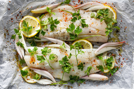 Fresh fish, cod fillets with parsley, lemon slices, onion and spices prepared for baking on parchment paper