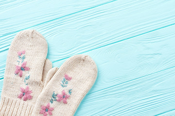 Pair of woolen mittens on wooden background. Female white knitted warm gloves on blue wooden background and copy space. New Year decoration and fashion.