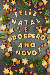 FELIZ NATAL COOKIES. Words Merry Christmas and Happy New Year en portuguese with baked cookies, Christmas decoration and nuts on black slate background. Christmas card for portuguese speaking