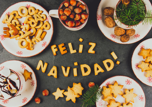 FELIZ NAVIDAD COOKIES. Words Merry Christmas en Spanish with baked cookies, Christmas decoration and nuts on black slate background. Christmas card for hispanic countries top view