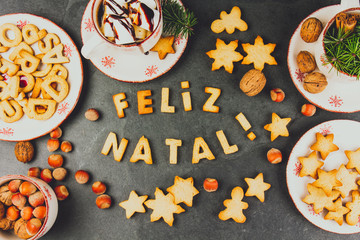 FELIZ NATAL COOKIES. Words Merry Christmas en portuguese with baked cookies, Christmas decoration and nuts on black slate background. Christmas card for portuguese speaking countries top view.