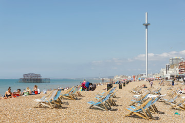 Fototapeta na wymiar Sunbathing people and deckchairs on the Brighton beach, West pier in the background