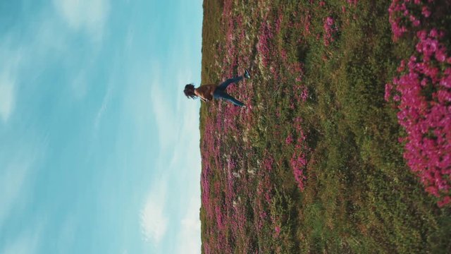 Rotation view of a young stylish teenage girl walking down the flowered mountain meadow. Fashionable look, stylish bomber and snickers Happy emotions, cheerful mood. Feeling free