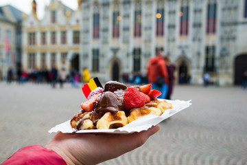 Belgium waffle with chocolate sauce and strawberries, Bruges city background