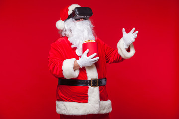 Santa Claus wearing virtual reality goggles and a red bucket with popcorn, on a red background. Christmas