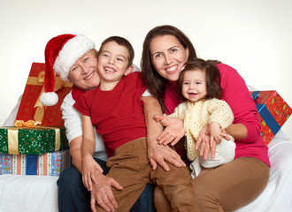 Grandma, daughter and grandchild dressed in santa hat with gift boxes sit on sofa, white background. New year eve and christmas holiday concept.