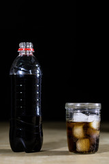 Soda and bottle on a wooden table. A glass and a bottle of beverage on the table.
