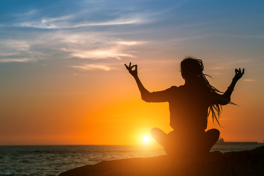 Yoga silhouette. Meditation woman on the ocean coast during amazing sunset. Healthy lifestyle.