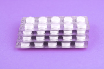 Packs of white pills packed in blisters with copy space on purple background. Focus on foreground, soft bokeh