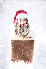 Happy cute fat Santa girl. Model in santa hat. XXL a woman celebrating Christmas and a new year. female is holding a present and small clock is an alarm clock. focus on the gift. with snowfall