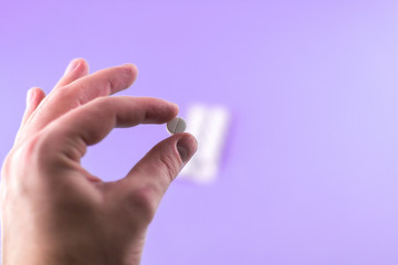 The man hand is holding a pill with copy space on purple background. Focus on foreground, soft bokeh