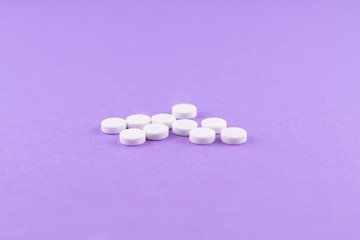 Fototapeta na wymiar White pills with copy space on purple background. Focus on foreground, soft bokeh