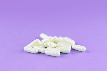 Close up white capsules on purple background with copy space. Focus on foreground, soft bokeh. Pharmacy drugstore concept