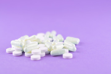 Obraz na płótnie Canvas Close up white pills and capsules on purple background with copy space. Focus on foreground, soft bokeh. Pharmacy drugstore concept