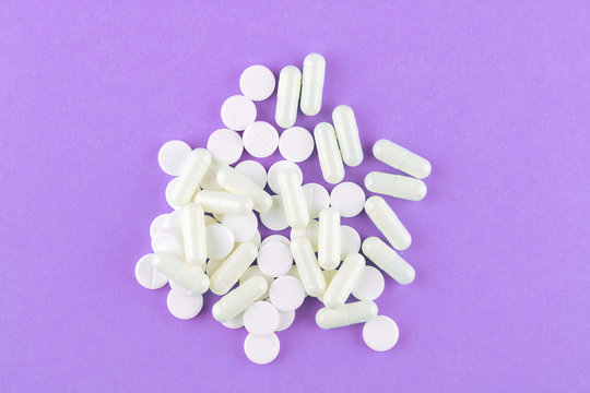 Close up white pills and capsules on purple background with copy space. Focus on foreground, soft bokeh. Pharmacy drugstore concept. Top view