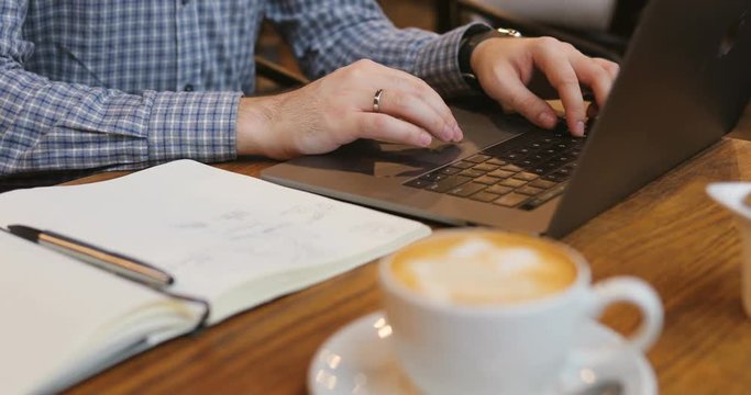 Close-up of a man's hand use laptop in the foreground of coffee and notebook in a cafe break businessman code business cup