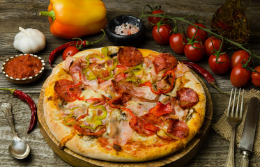 Pizza with pepperoni, ham and peppers on dark wood background. Hot homemade delicious pizza