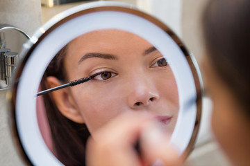 Woman putting mascara in ring light round makeup mirror at home bathroom morning routine. Beautiful...